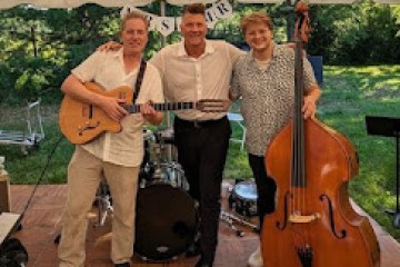 Three musicians with guitar, drum, and double bass under a tent outdoors.