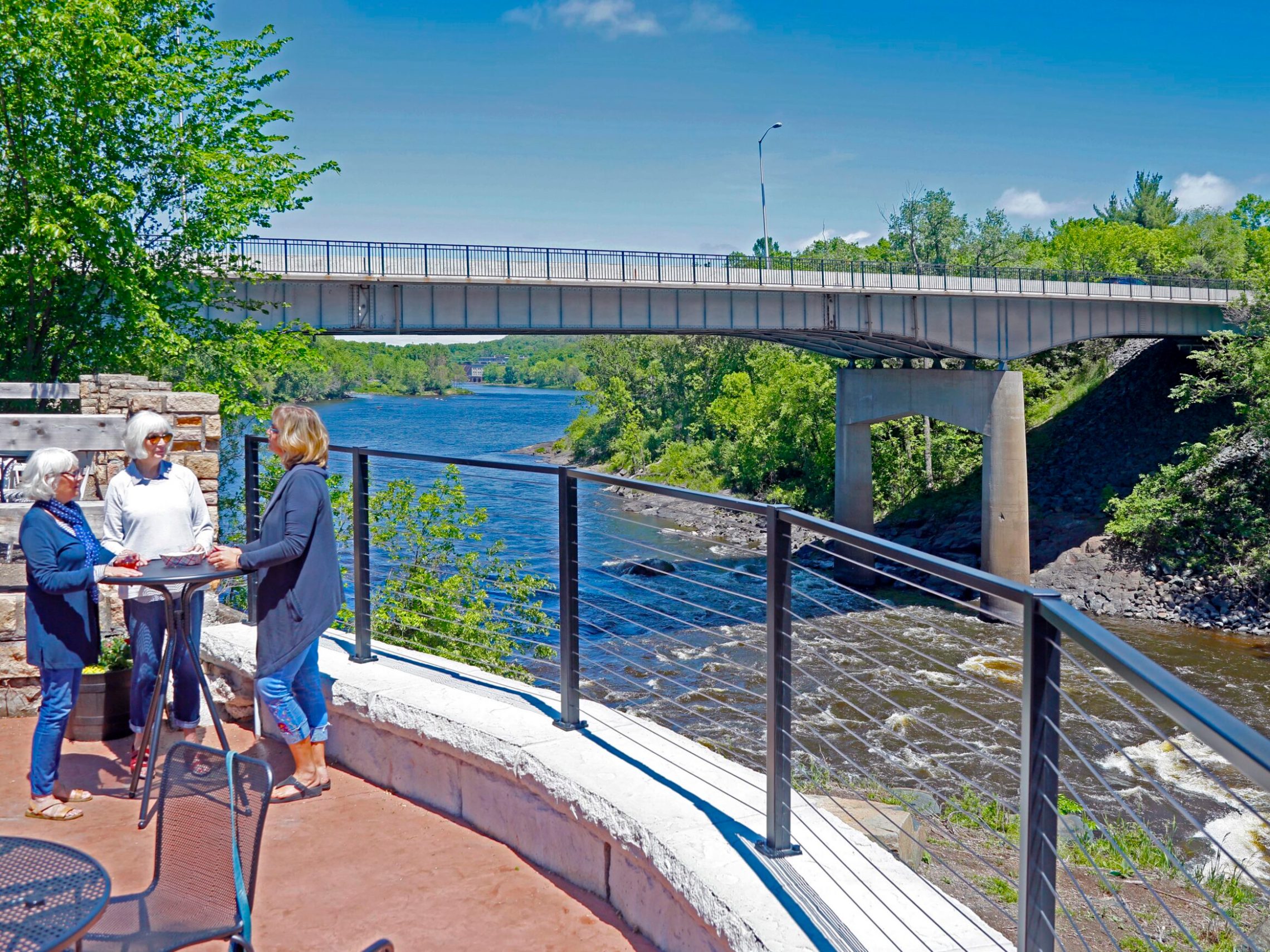 women standing on a patio in front of a bridge