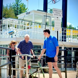 Older man with walker assisted on boarding a boat ramp by a staff member in blue shirt.