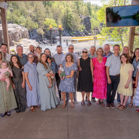 Group of 24 people posing under a pavilion near a scenic outdoor area.