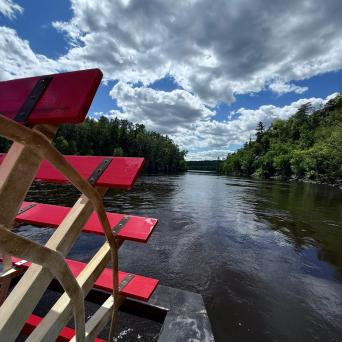 Red paddle wheel and river with cloudy sky and trees on a sunny day.