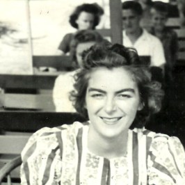 Smiling woman in striped blouse sitting with people in a train or tram.