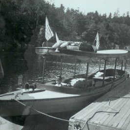 Vintage boat docked with flags on a lake, surrounded by trees.