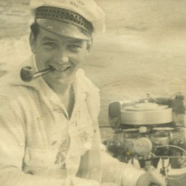 Vintage photo of a smiling man in a sailor hat with a pipe, sitting beside machinery.