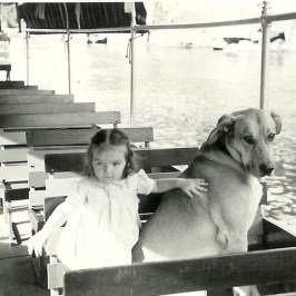 Child in white dress and large dog sitting on a boat with empty seats.