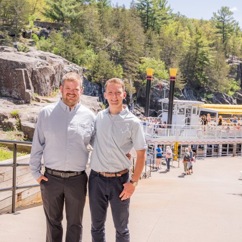 Two men standing on a path near a boat docked by rocky cliffs.