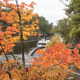 Boat on river surrounded by vibrant autumn trees.