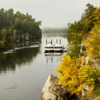 Riverboat on a misty river surrounded by autumn foliage.