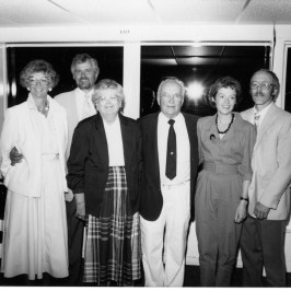 Group of six adults posing indoors, dressed in formal attire.