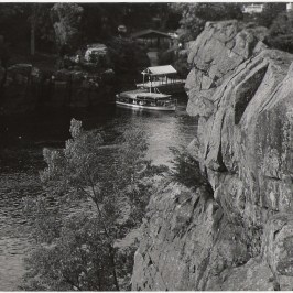 Boat on river surrounded by rocky cliffs and trees.