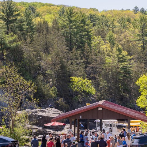 People gathered at a small pavilion with trees and a hill in the background.