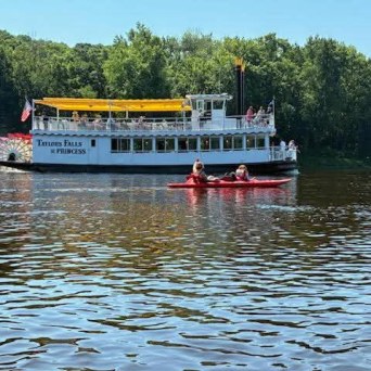 River scene with a ferry boat and people kayaking nearby.