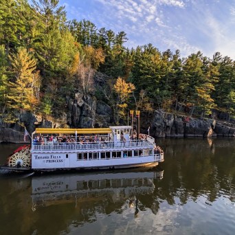 Tour boat on a river with forested cliffs in autumn.