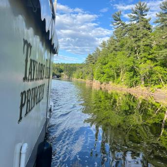 Boat on river with scenic forest and blue sky view.