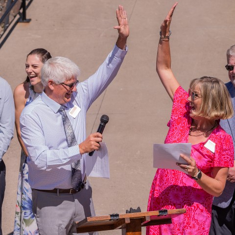 Man and woman high-five at outdoor event podium, surrounded by onlookers.