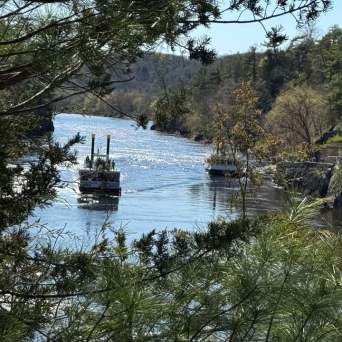 Two boats on a scenic river surrounded by trees and rocky cliffs.