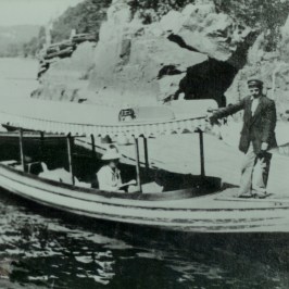 Vintage photo of a man and woman on a small boat near rocky shore.