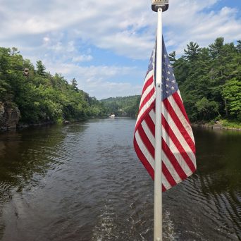 American flag on a boat with river and trees in the background.