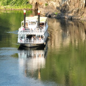 Paddle steamboat on a calm river near rocky cliffs.