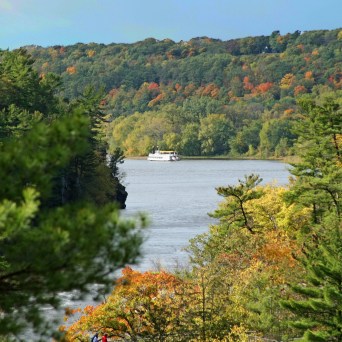 River with a boat surrounded by forest with autumn foliage.