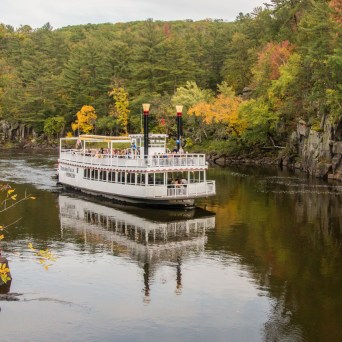Paddleboat cruising on river with autumn trees on both sides.