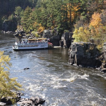 Boat cruising through a river canyon with autumn foliage.
