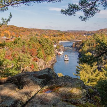 River with bridge and boat surrounded by autumn trees and rocks.